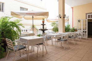 An outdoor patio area with tables and chairs, umbrellas, and potted plants.