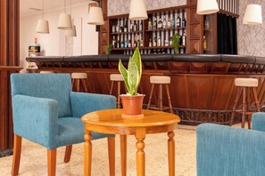 Zona de bar con mostrador de madera, sillas tapizadas en azul y una mesa redonda de madera con una planta en maceta.
