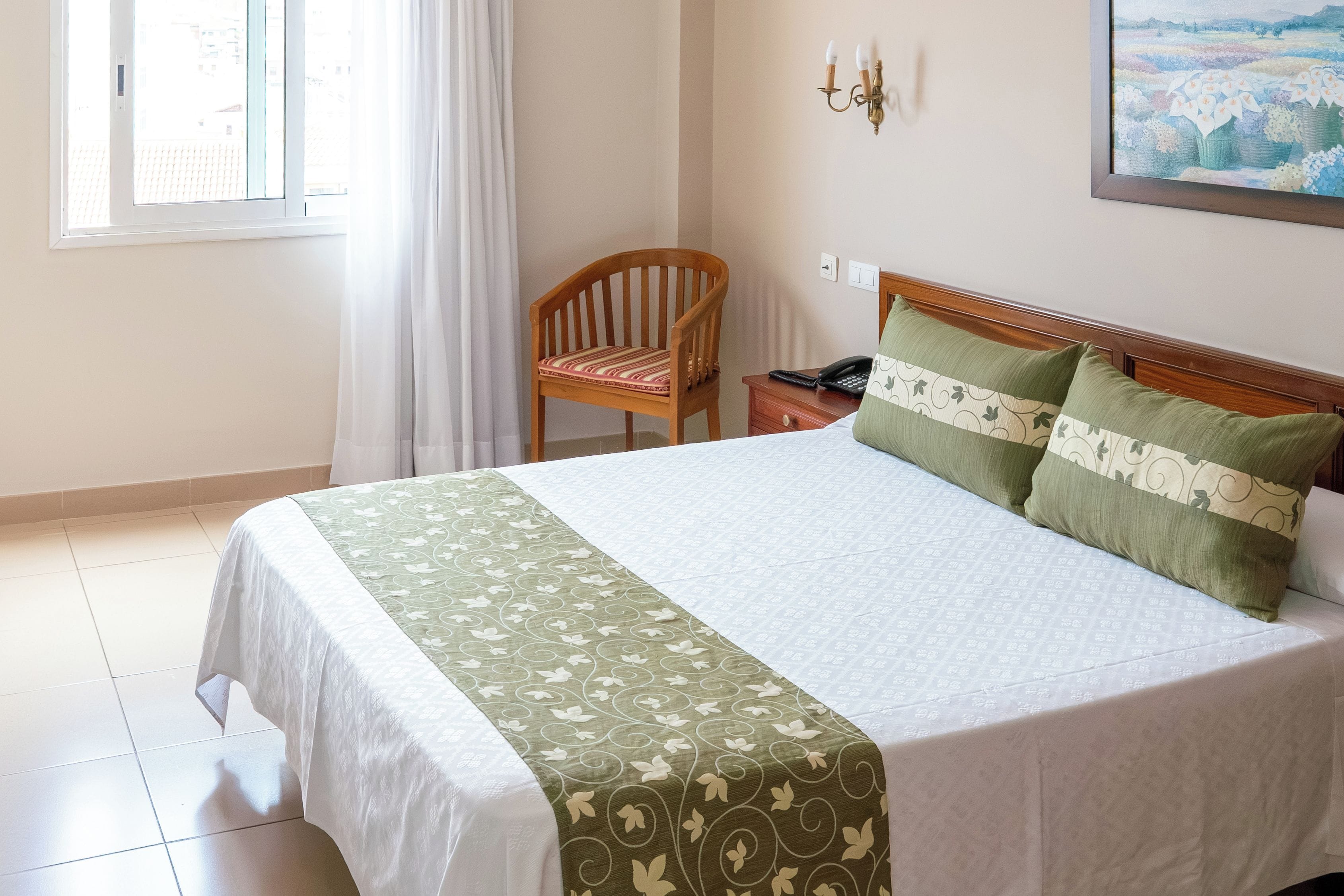 Een hotelkamer met een bed, een stoel, een nachtkastje met een telefoon en een schilderij aan de muur.