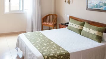 Een hotelkamer met een bed, een stoel, een nachtkastje met een telefoon en een schilderij aan de muur.