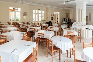 Un comedor de hotel con varias mesas y sillas, un reloj en la pared y un televisor al fondo.