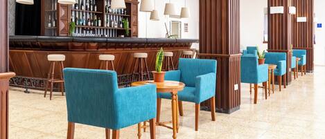 A bar area with a long counter, multiple hanging lamps, and a row of blue chairs with wooden legs.