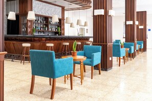 Eine Bar mit einer langen Theke, mehreren hängenden Lampen und einer Reihe blauer Stühle mit Holzbeinen.