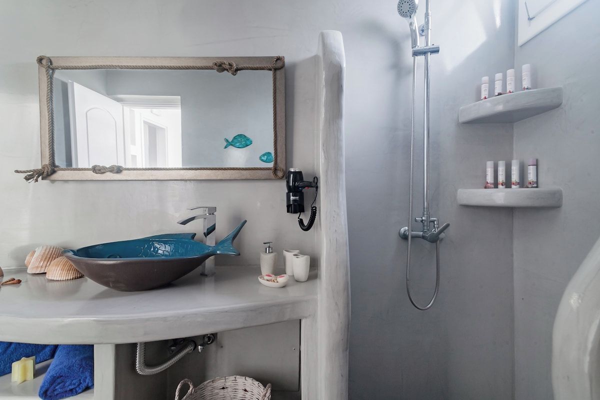 Ein Badezimmer mit einem runden Waschbecken, einem Spiegel mit Ropeschrank, einer Dusche und einem Ablagebereich für Pflegeprodukte.