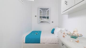 Ein kleiner, weißer Raum mit einem Bett, einem Fenster mit Meerblick und einem Tisch mit Kuchen und Dekoration.