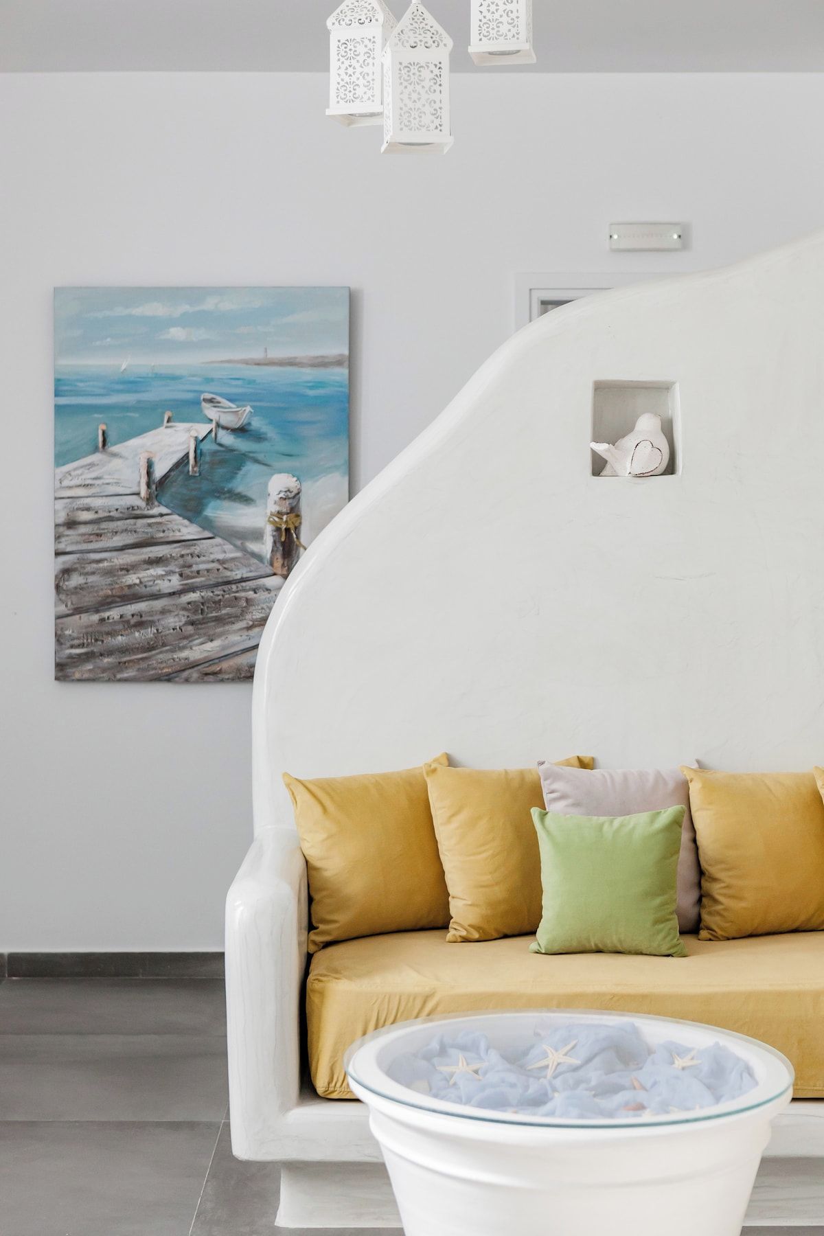 Ein modernes Wohnzimmer mit einem weißen Sofa, einem Glastisch und einem Gemälde einer Küstenlandschaft.