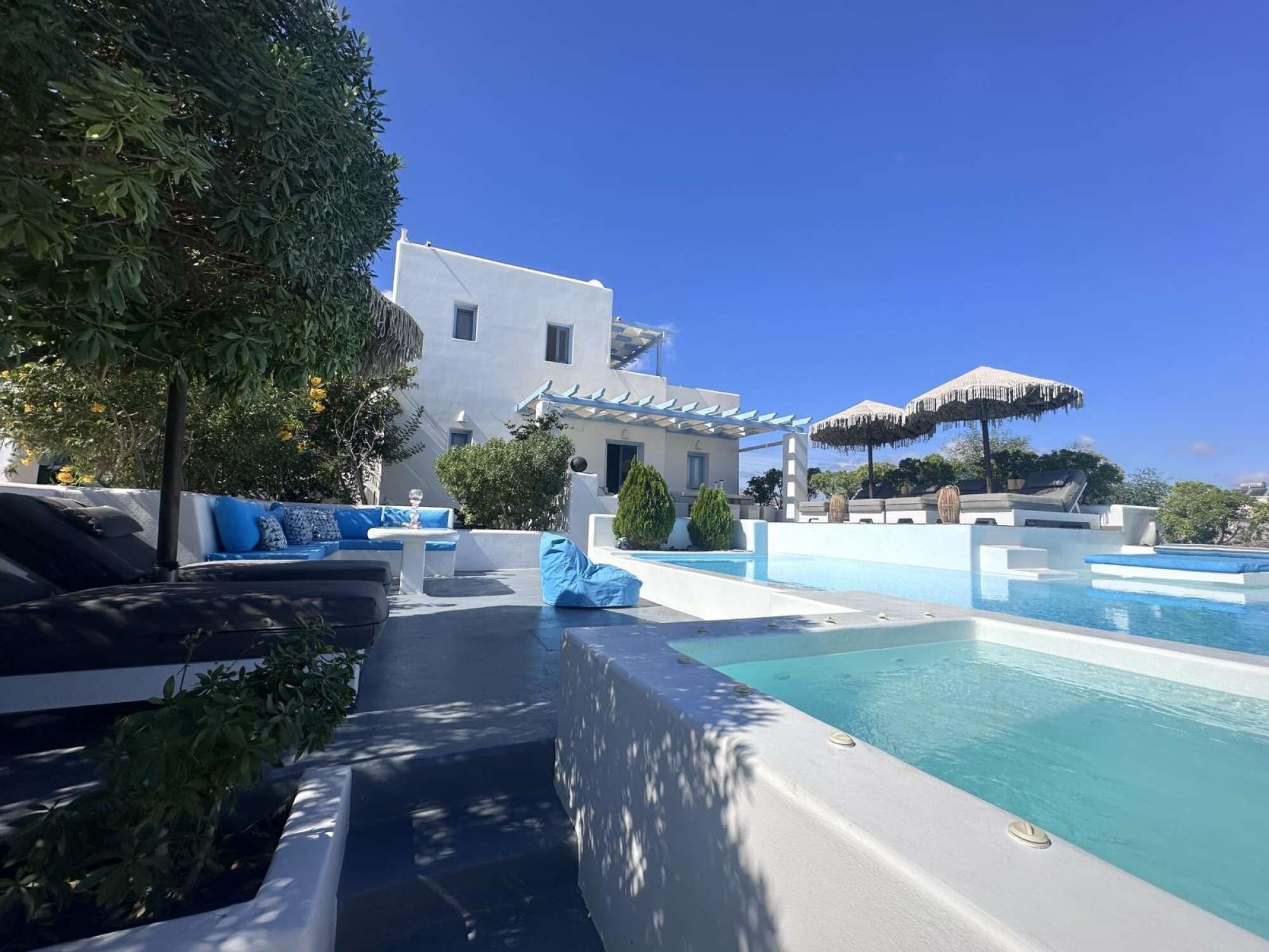 A pool area with a modern pool, lounge chairs, and a white building in the background.