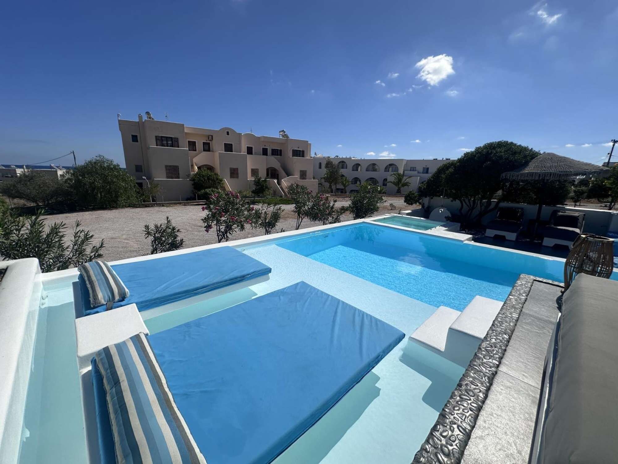 A swimming pool with multiple lanes, surrounded by lounge chairs and umbrellas, with a building in the background.