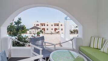 Ein Balkon mit einem weißen Stuhl, einem runden Tisch mit grüner Tischdecke und Blick auf ein Gebäude mit Bögen und einem Pool.