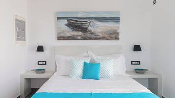 Ein Schlafzimmer mit einem Bett, zwei Nachttischen, einem Bild von einem Boot am Strand und einem Fenster.