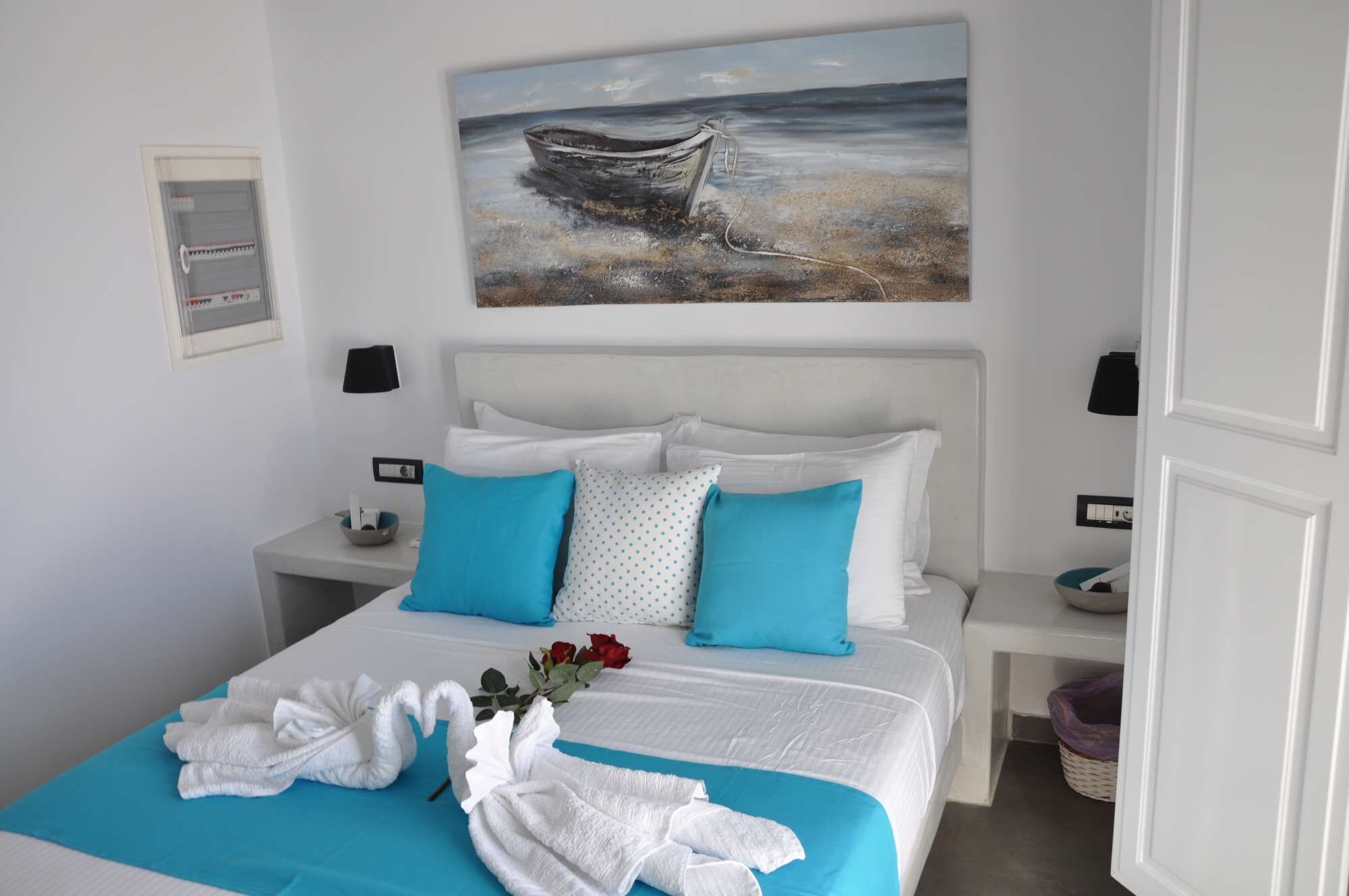 Ein Hotelzimmer mit einem Bett, zwei Nachttischen, einem Bild eines Bootes an der Wand und einer Vase mit Blumen auf dem Bett.