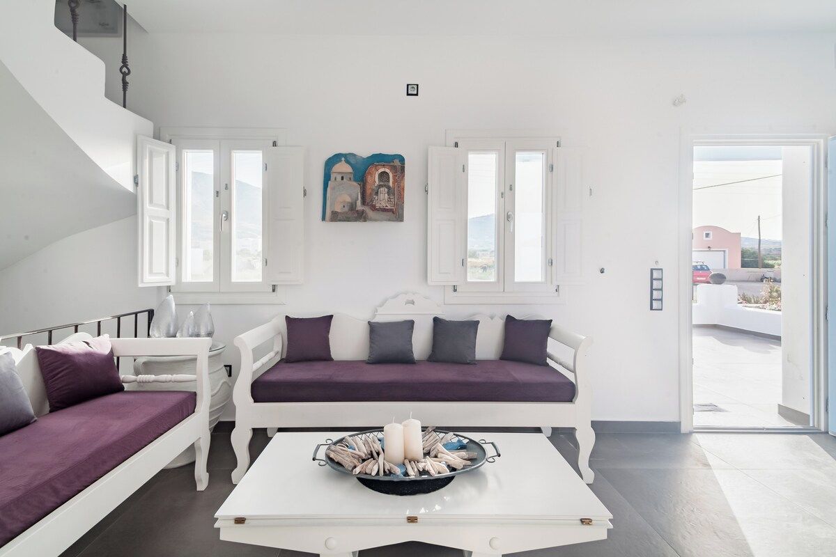 Ein modernes Wohnzimmer mit einem weißen Sofa, einem weißen Couchtisch mit Kerzen und einem Gemälde über dem Sofa.