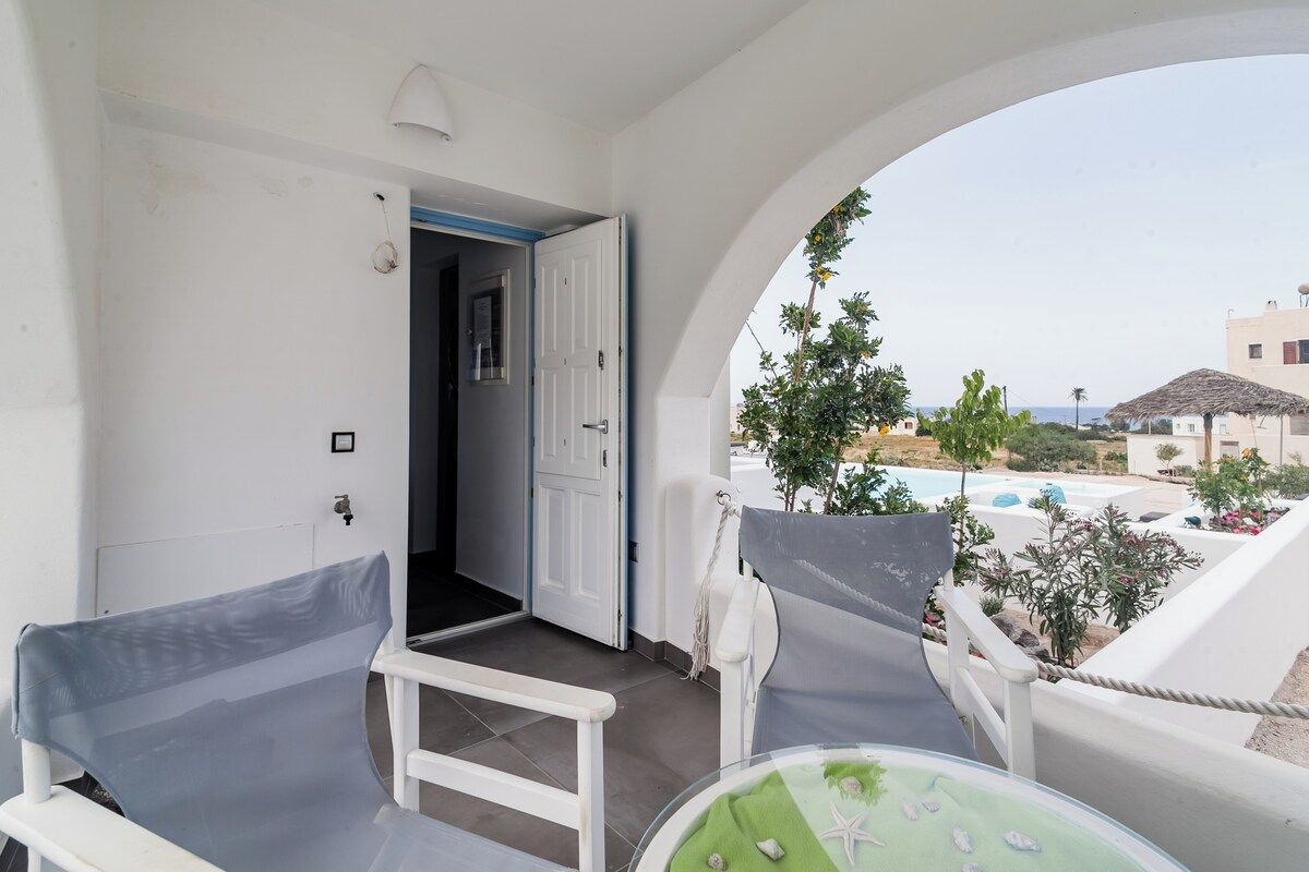 Ein Balkon mit weißem Stuhl, einem kleinen Tisch und Blick auf einen Pool sowie Gebäude.