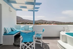 A terrace with a white and blue color scheme, featuring a round table, chairs, and a seating area with cushions.