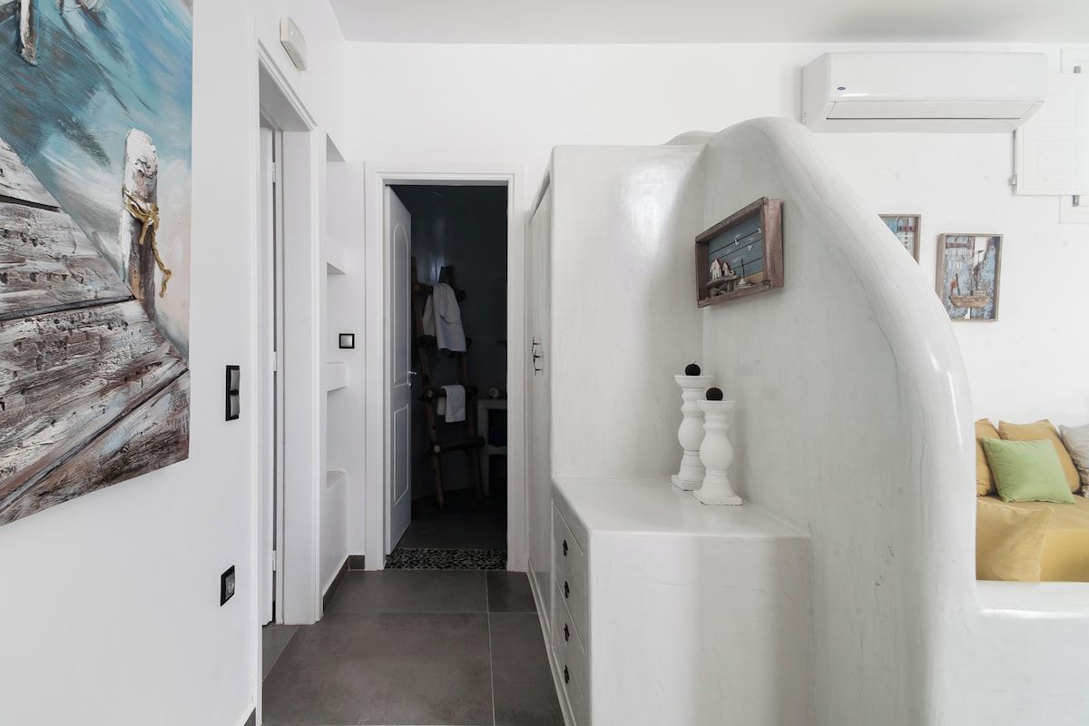 Ein Korridor mit weißer Wand, einem hölzernen Kunstwerk, einer weißen Bank und einer Tür zu einem Zimmer.