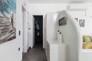 Passadís amb una paret blanca, una obra d'art de fusta, una banca blanca i una porta que dona a una habitació.