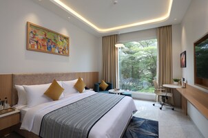 Habitación de hotel con una cama grande, un escritorio, una silla, una ventana con vistas a árboles y un cuadro en la pared.