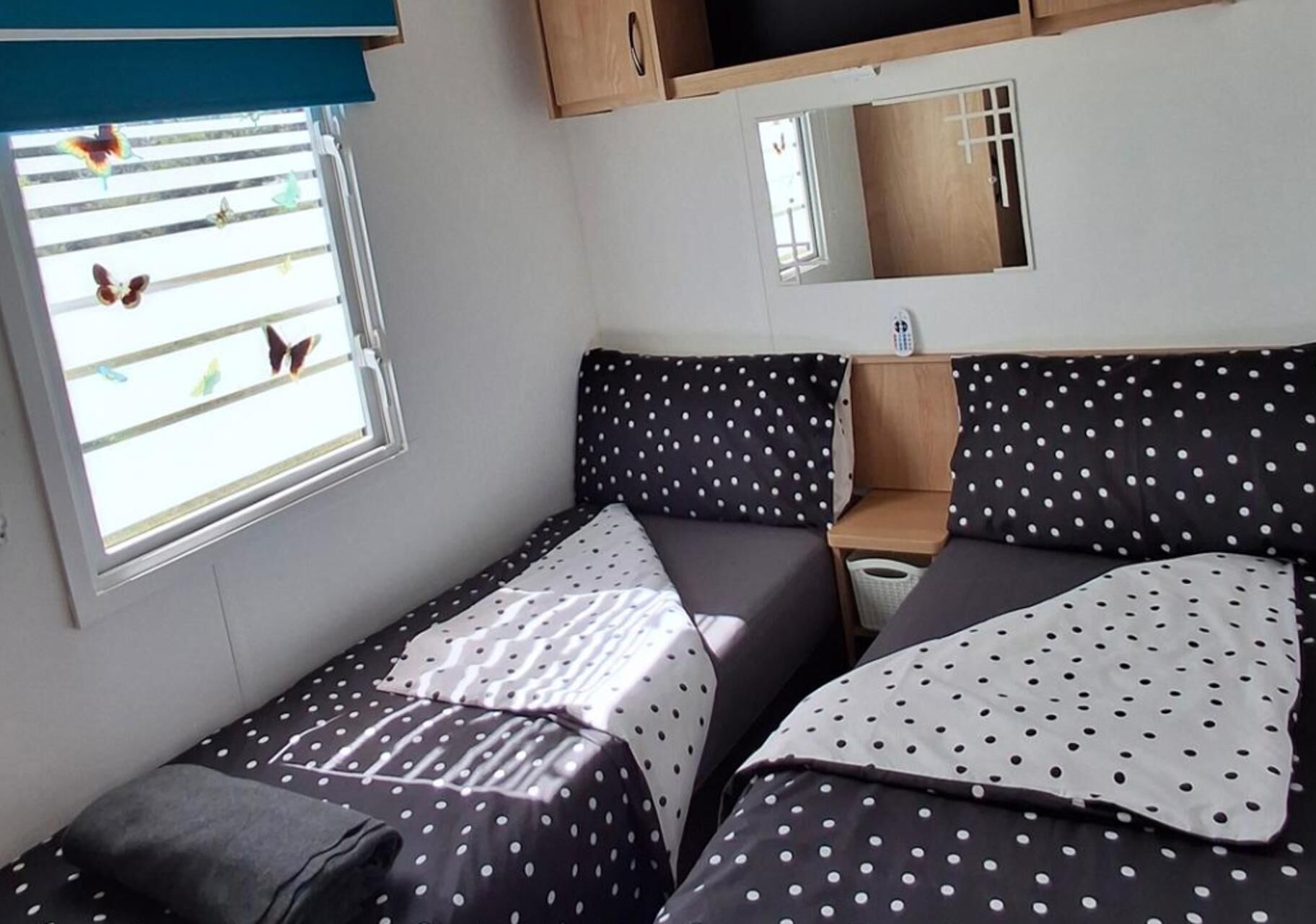 A small, compact room with a bed, a bedside table, and a window with butterfly decals.