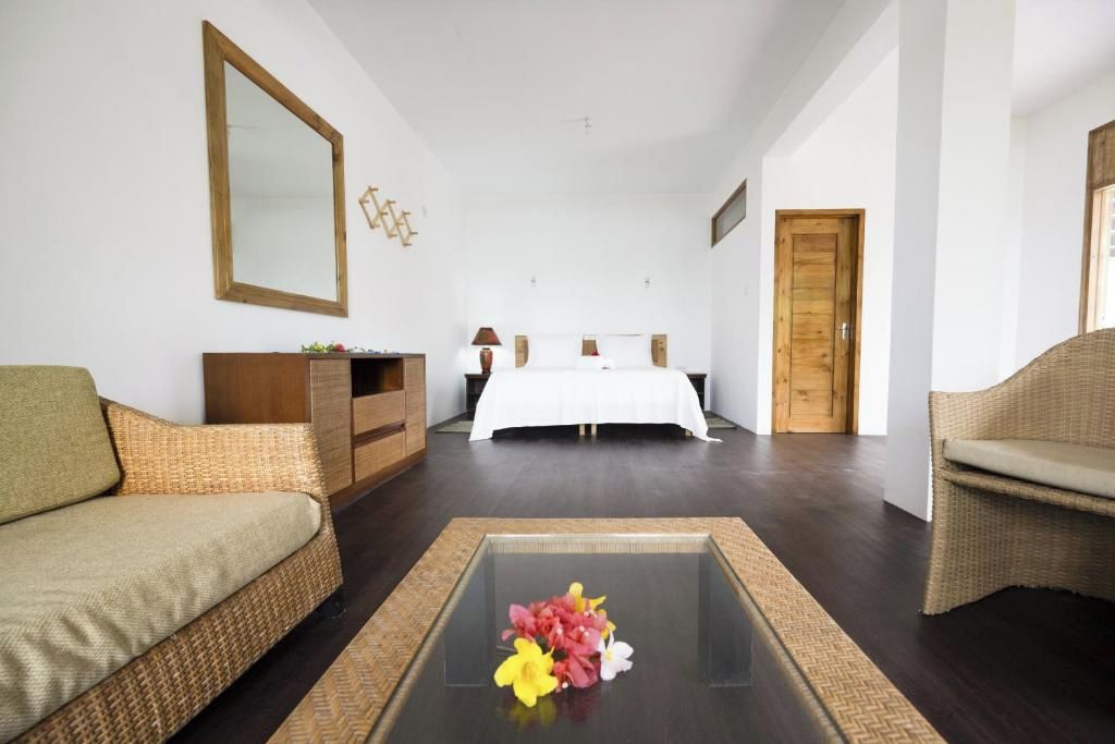 A hotel room with a bed, a sofa, a coffee table with flowers, a dresser, and a mirror.