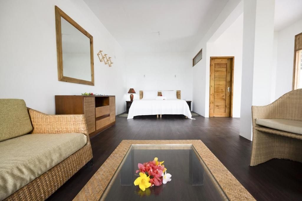 A hotel room with a bed, a sofa, a coffee table with flowers, a dresser, and a mirror.
