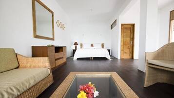 A hotel room with a bed, a sofa, a coffee table with flowers, a dresser, and a mirror.