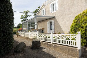 Een huis met een overdekte patio, een wit hek en een grindpad.