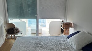 Una camera da letto con un letto grande, una sedia, un tavolino e vista mare tramite una porta scorrevole.