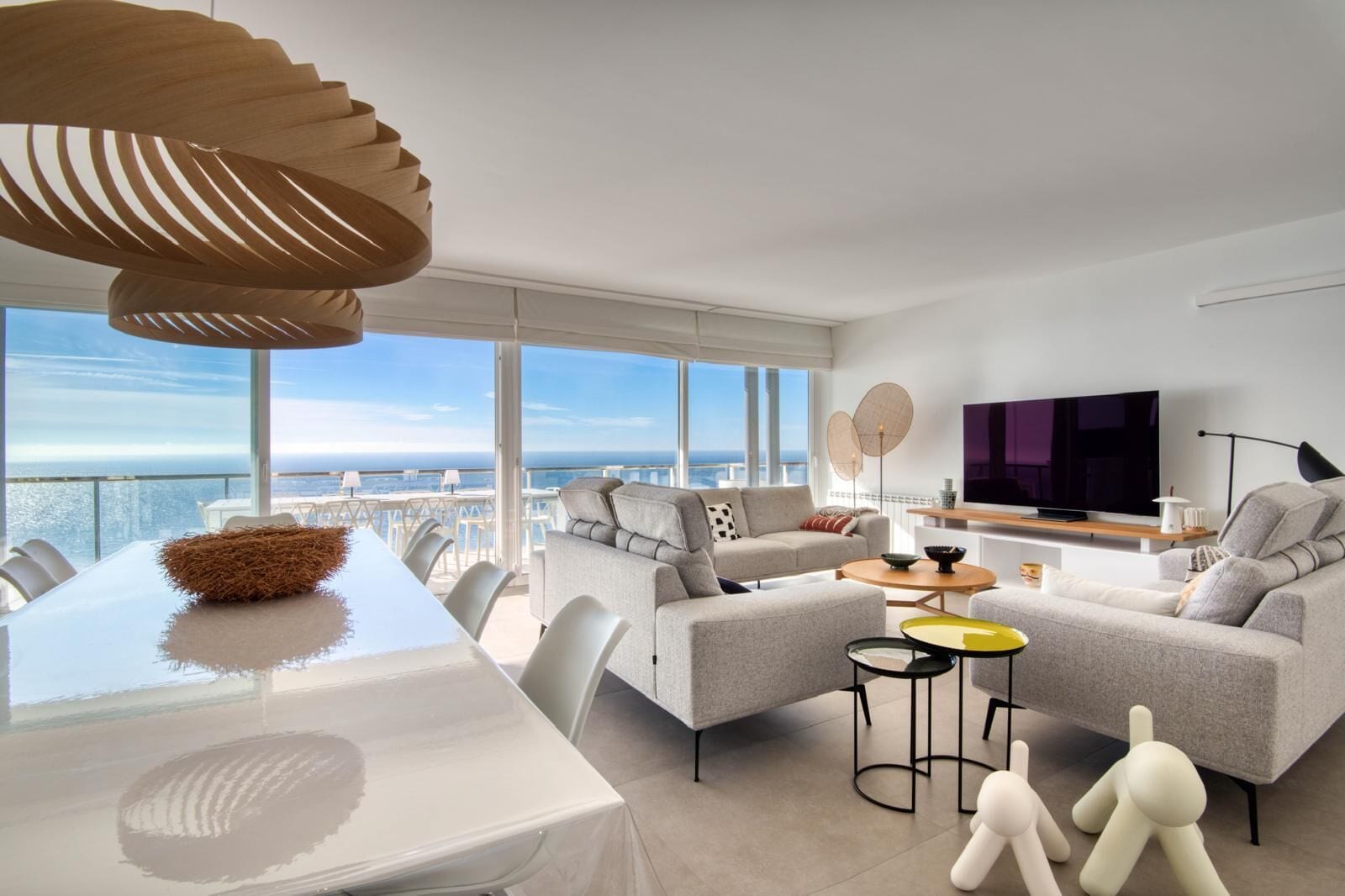 A modern living room with a sofa, TV, and dining area, overlooking a scenic view.