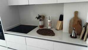 Un piano di lavoro da cucina con un tagliere nero, un sottopiattino intrecciato, un portacoltelli, un tagliere in legno e un boccale di metallo.