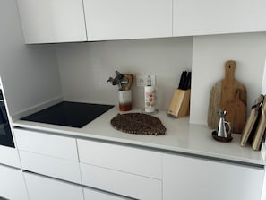 Eine Küchenarbeitsplatte mit Schneidebrett, gewebter Unterlage, Messerblock, Holzschneidebrett und Metallkanne.