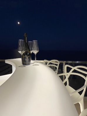 Ein Tisch mit einer Flasche und Gläsern vor einem Nachthimmel mit sichtbarem Mond.