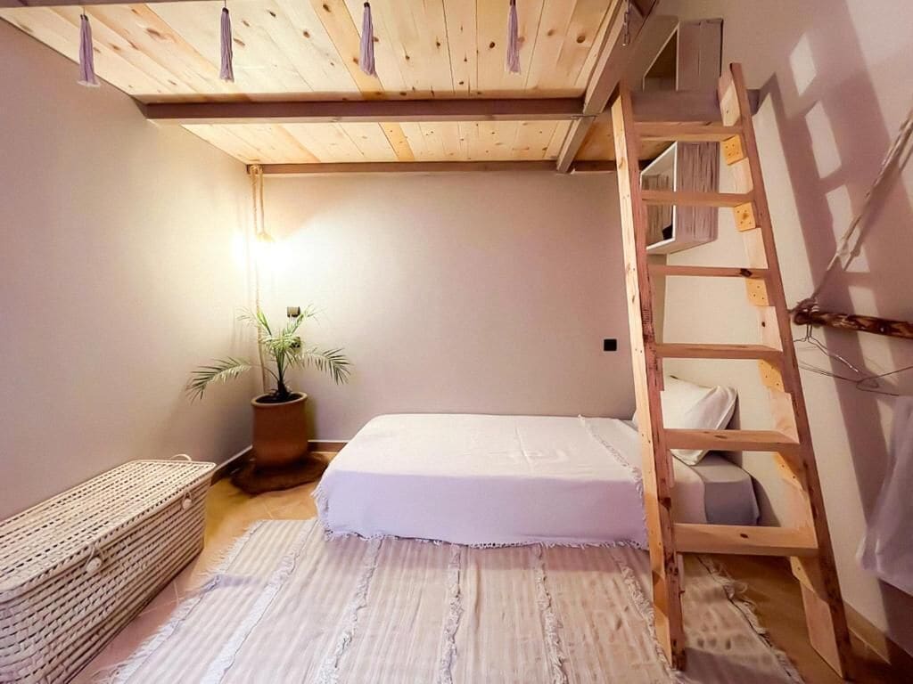 A bedroom with a bunk bed, a bedside table, a potted plant, and a woven basket.