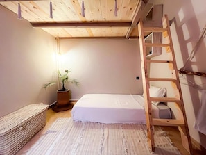 Un dormitorio con una cama litera, una mesita de noche, una planta en maceta y una cesta tejida.