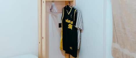 A small room with a bed, a wooden wardrobe, a towel, and a hanging garment.