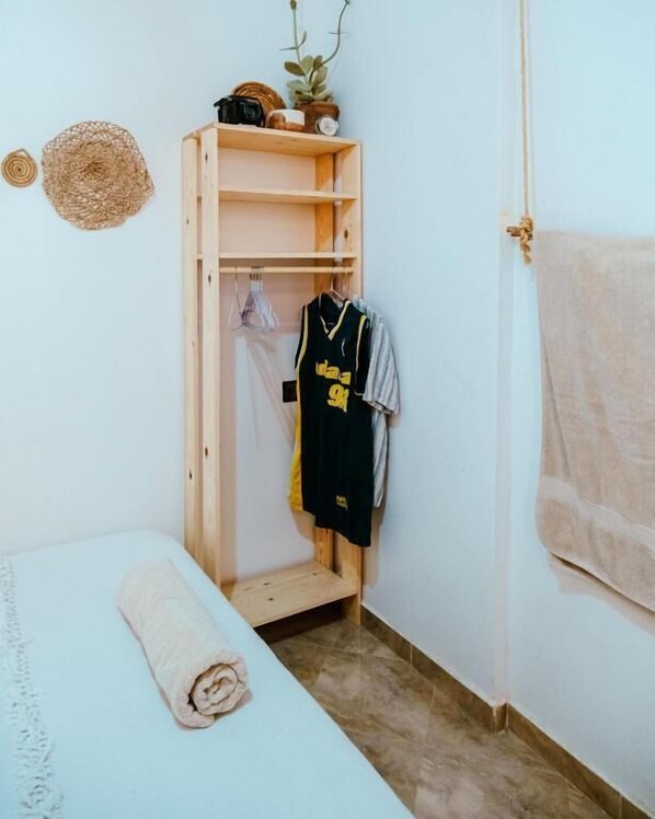 A small room with a bed, a wooden wardrobe, a towel, and a hanging garment.
