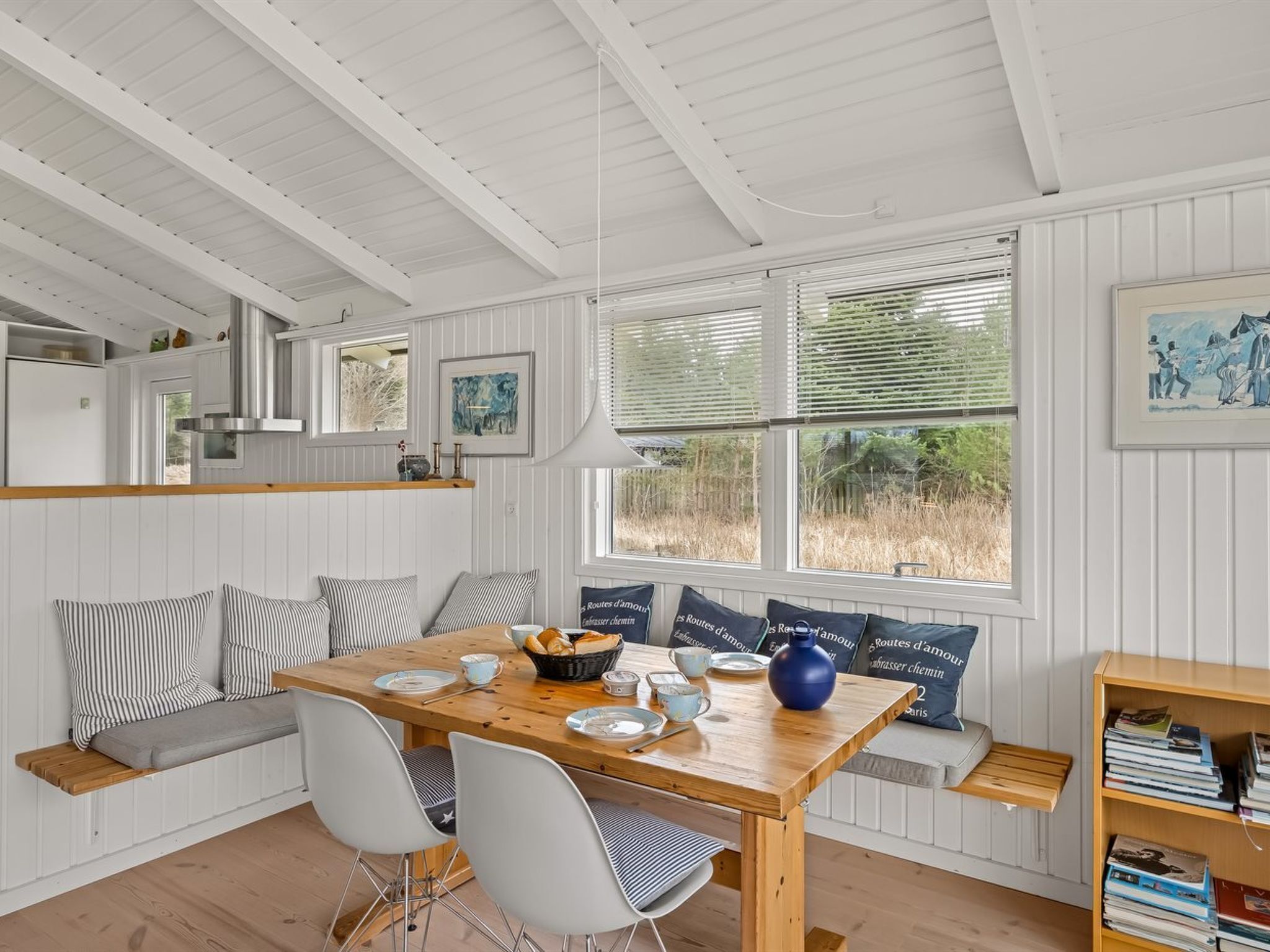 A cozy dining area with a wooden table, white chairs, and a bench with striped cushions.