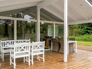 Ein überdachter Außenbereich mit Holzterrasse, weißen Möbeln und Glasüren zum Innenraum.