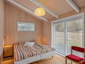 A bedroom with a bed, a nightstand, a chair, a window with blinds, and a hanging light fixture. - "Gudmunda" - 300m from the sea by Interhome (Jerup)