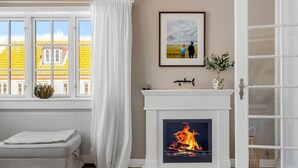Una sala de estar con chimenea, un sofá, una ventana con cortinas y un cuadro en la pared.