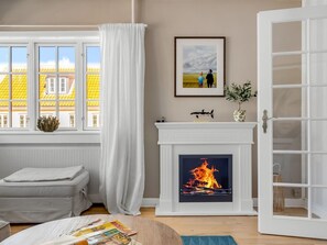 A living room with a fireplace, a sofa, a window with curtains, and a framed picture on the wall. - "Annagrete" - 300m from the sea by Interhome (Skagen)