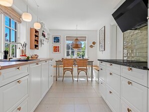 A kitchen with white cabinetry, a dining table with chairs, pendant lights, and artwork on the walls. - "Annagrete" - 300m from the sea by Interhome (Skagen)