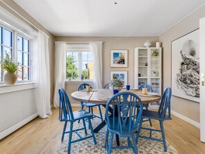 A dining area with a round table, blue chairs, a white cabinet with glassware, and a large framed artwork on the wall. - "Annagrete" - 300m from the sea by Interhome (Skagen)