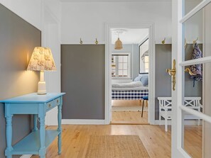 A hallway with a blue table and lamp, a door leading to a bedroom with a checkered bedspread, and a hanging light fixture. - "Annagrete" - 300m from the sea by Interhome (Skagen)