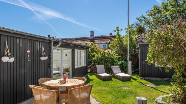Un patio con mobiliario de mimbre, una pequeña mesa y una puerta de vidrio que da a un jardín.