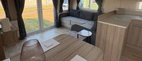 A compact living space with a kitchenette, a sofa, a dining table, and a large window with curtains.