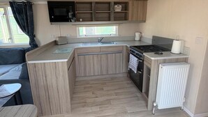 A compact kitchen with a microwave, stove, and sink. - Billing Aquadrome 2-bed Caravan, Sleeps 6, Parking (Northampton)