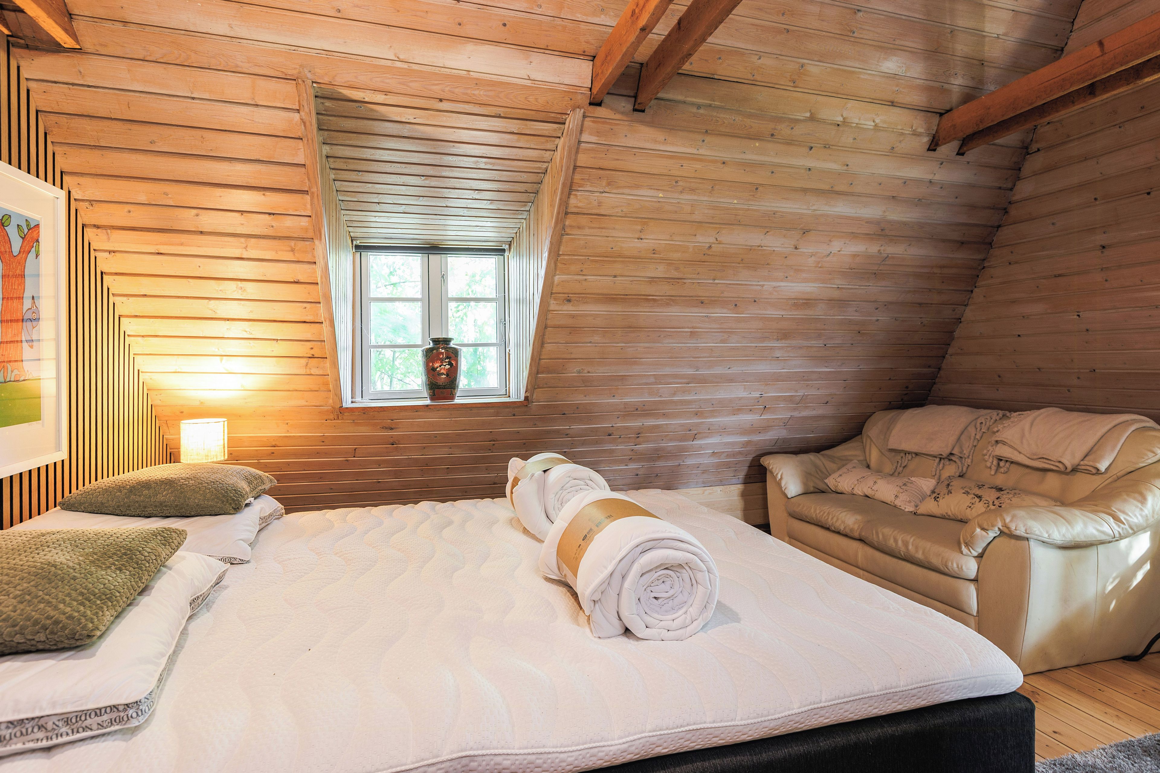 Une pièce confortable avec un lit, une fenêtre, une chaise et un tableau accroché au mur.