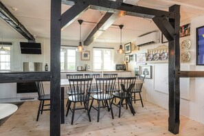 Comedor con mesa y sillas de madera, cocina al fondo y vistas al exterior.