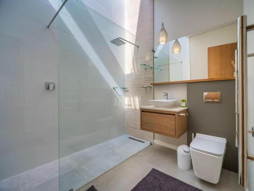 A modern bathroom with a glass shower enclosure, a wooden vanity, a white sink, and a large mirror.