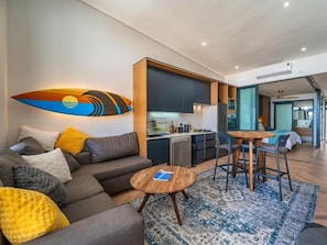 A modern living room with a sofa, coffee table, and a kitchen area visible in the background. - Kabeljauws Beachfront Luxury Apartments (Jeffreys Bay)